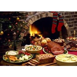 Et festligt julemåltid med forskellige retter, brød, skinke, ost og frugt foran en pejs med strømper og et pyntet juletræ.